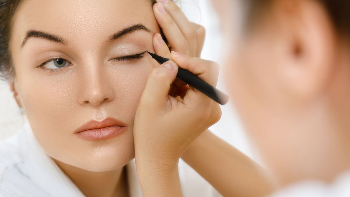 30_year_old_lady_applying_black_felt_tip_type_eyliner_in_bathrobe_on_closed_eye_upper_eyelid