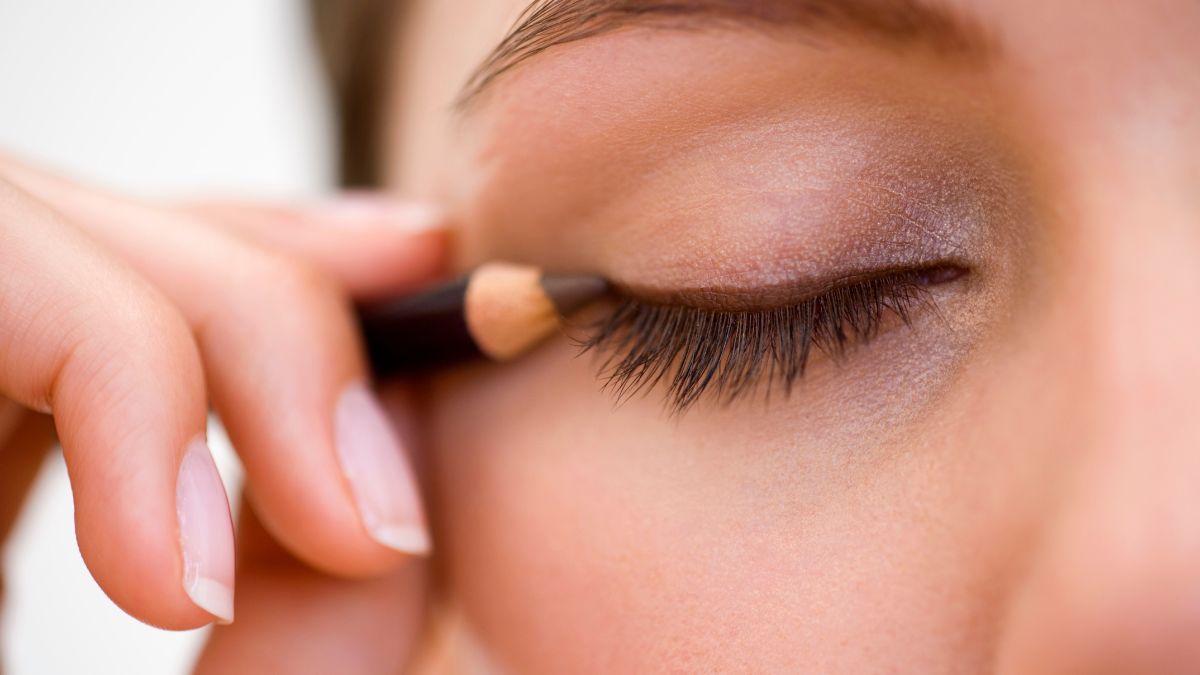 30_year_old_lady_applying_brown_pencil_eyliner_on_closed_eye_upper_eyelid