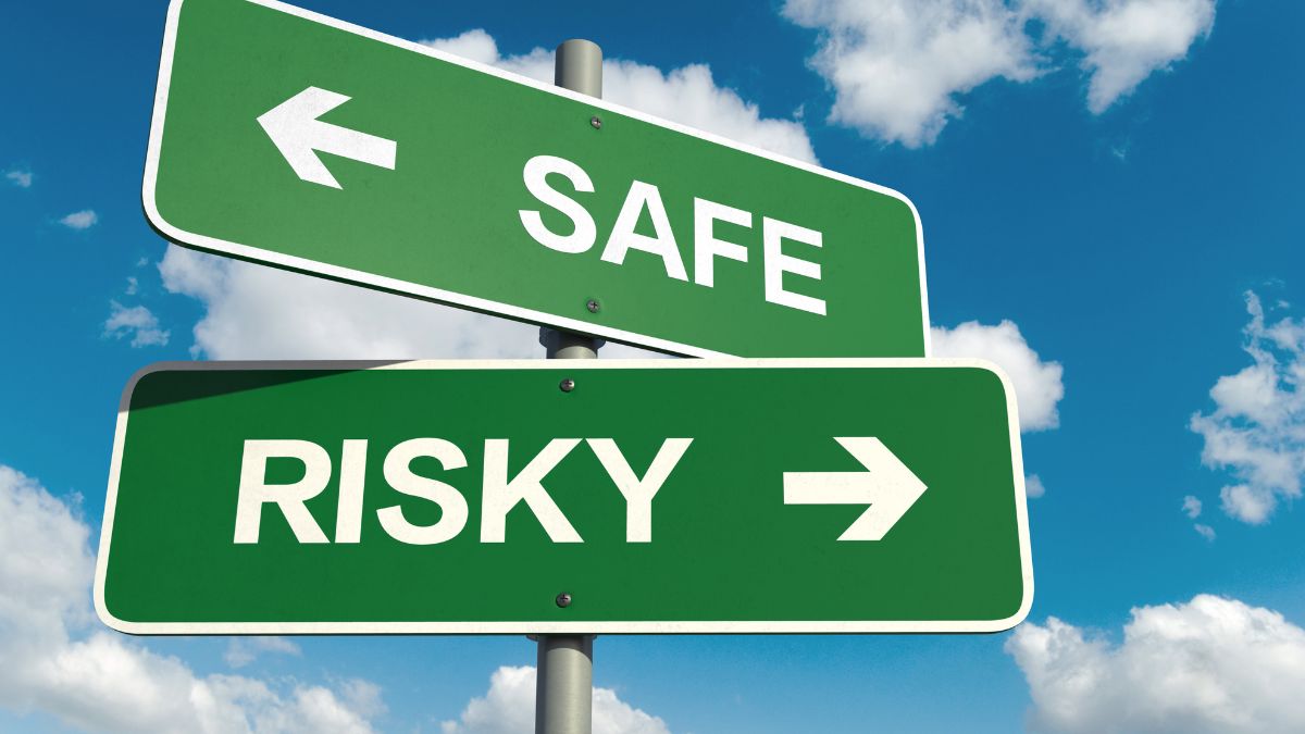 A_green_sign_with_white_writing_indicating_safe_in_one_direction_and_risky_in_the_other._clouds_in_the_sky_as_the_background.
