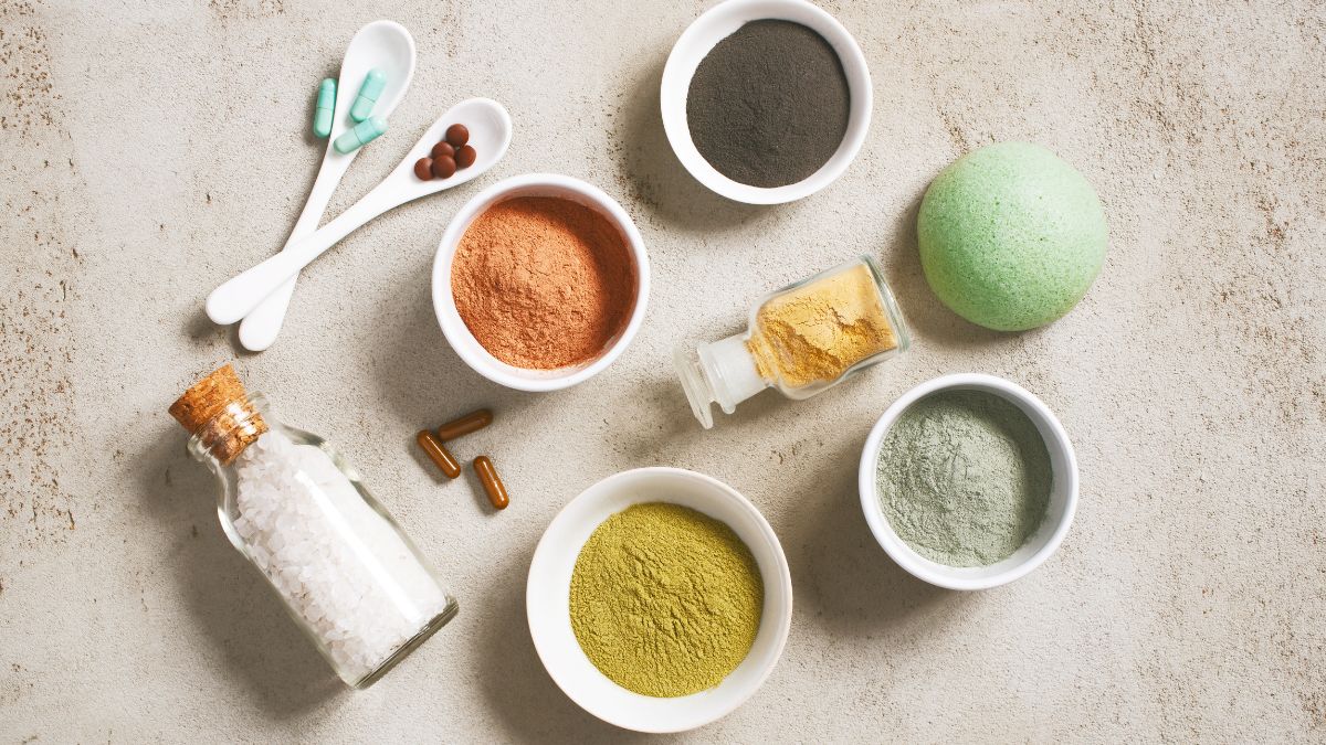 Cosmetic_ingredients._Colourful_powders_in_bowls._Light_orange_light_green_powders_and_bottle_lying_on_a_light_grey_table.