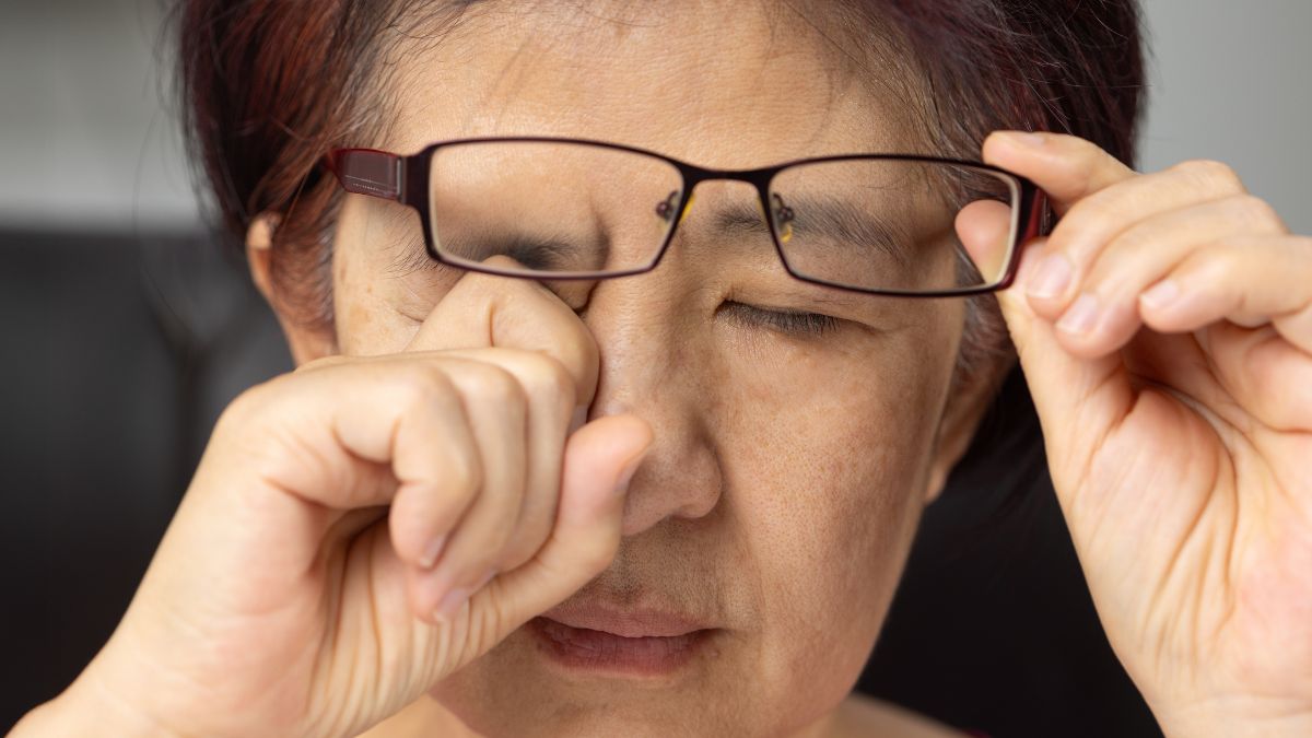 Dry itchy irritated eyes 50 year old lady lifting glasses and rubbing one eye while eyes are closed. in a room. daytime.